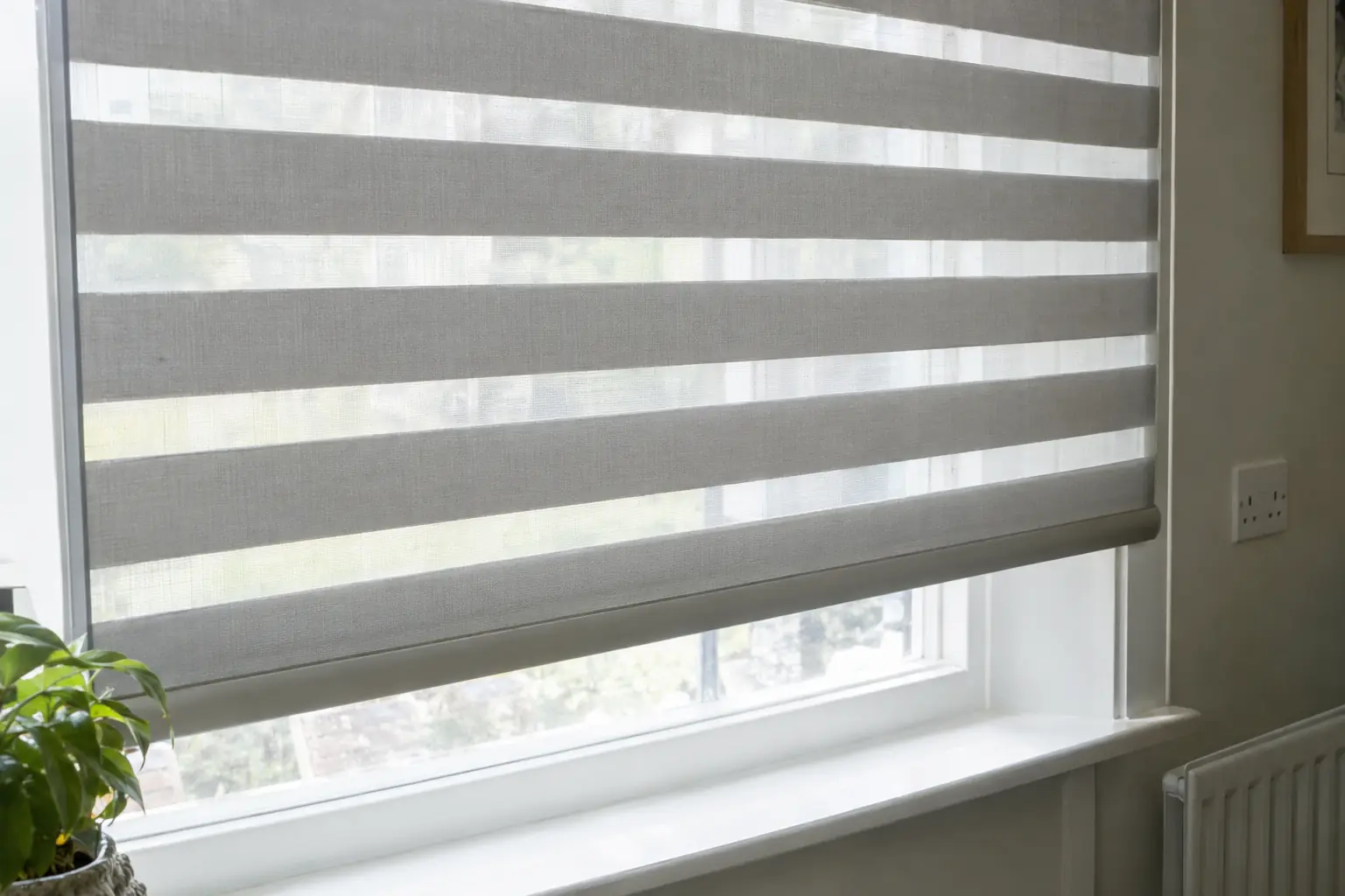 a close view of the bottom of a day and night blind, the two layers of fabric looping round the bottom bar, sheer and solid bands partly offset to make a fine striped screen against bright daylight