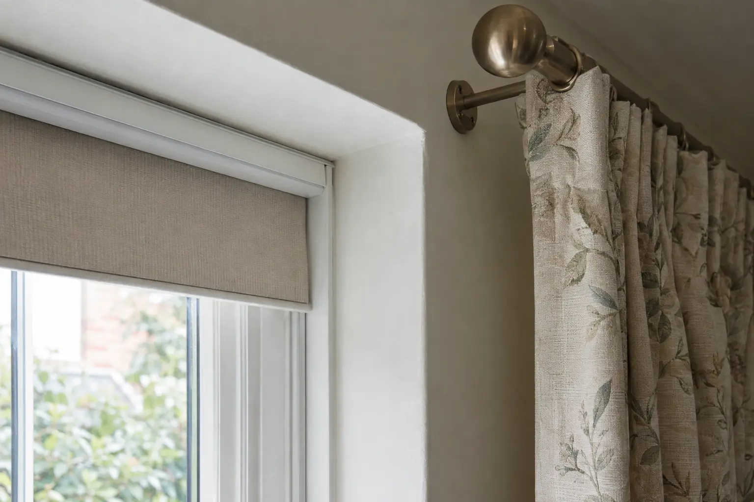 a close side-on view at the corner of a window showing the depth of the plaster reveal, a blind headrail tucked inside it and a curtain pole bracket fixed to the wall just outside