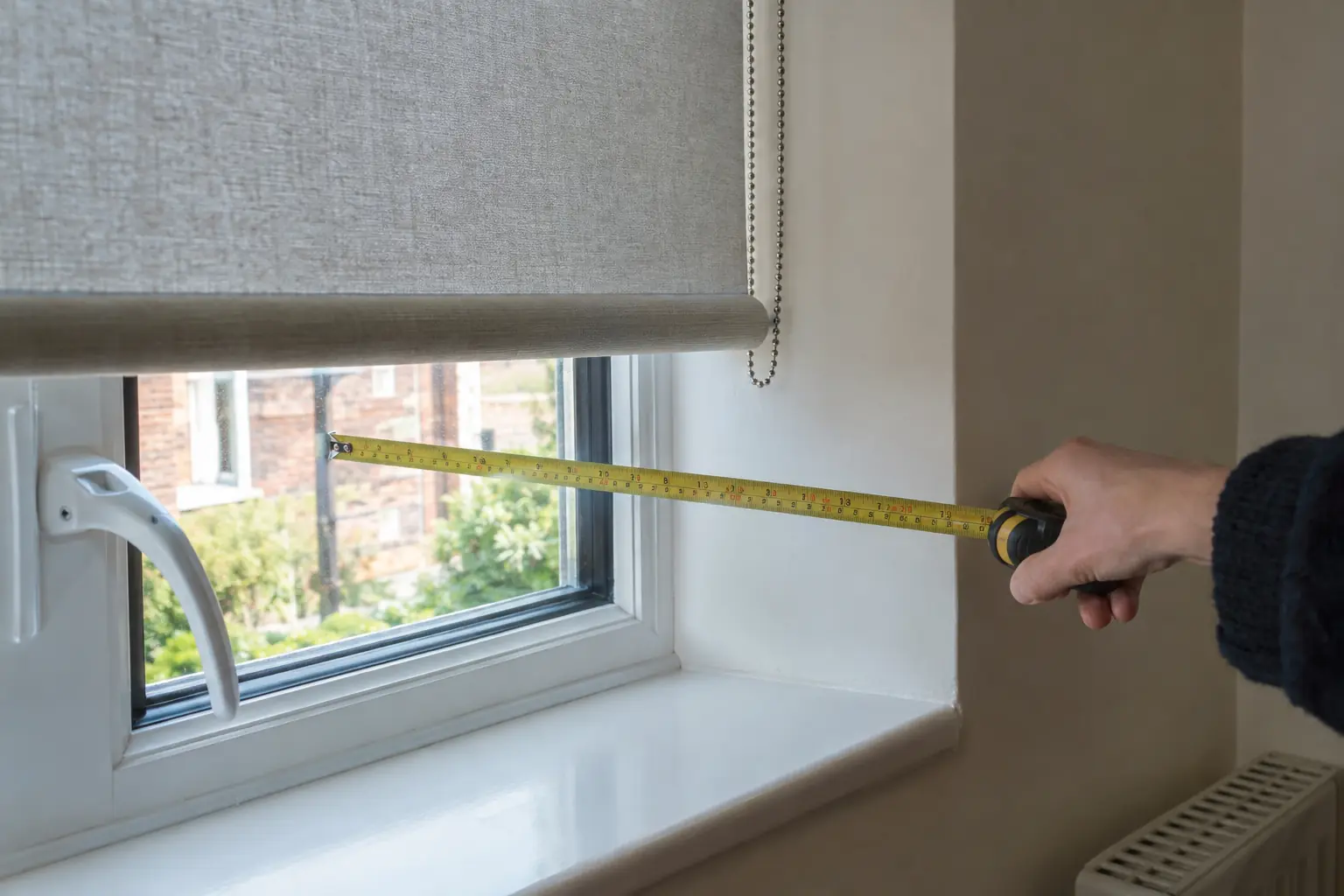 a close view of a window reveal with a tape measure extended from the glass to the front edge of the plaster reveal, a window handle projecting into the space