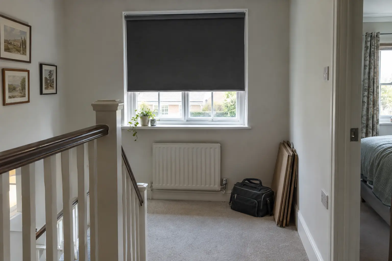 a newly fitted charcoal roller blind at a landing window in a 1930s semi, a closed toolbag on the floor and flattened cardboard packaging stacked neatly beside it